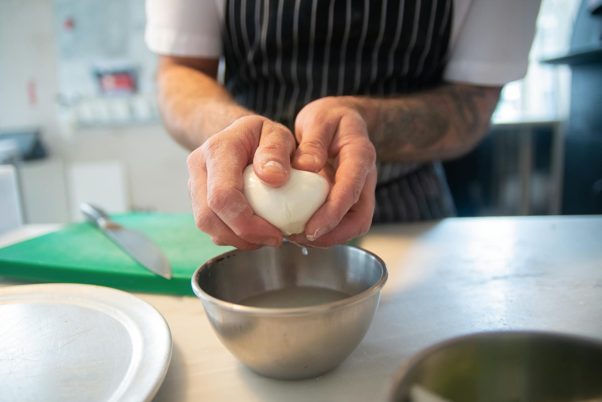 Close-up of a chef squeezing mozzarella cheese over a bowl in a kitchen setting.