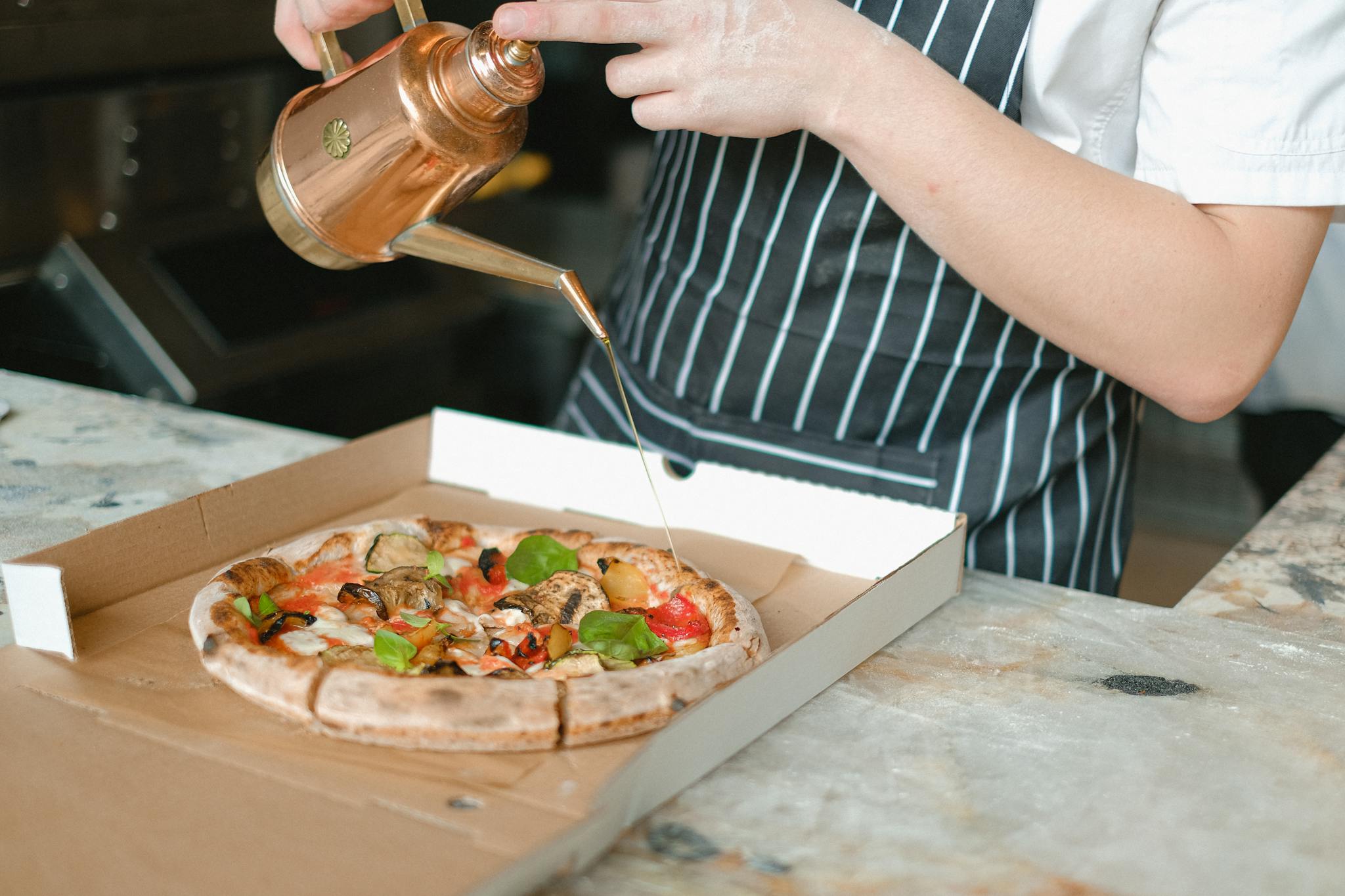 Close-up of chef adding olive oil to a fresh pizza in a pizzeria kitchen.