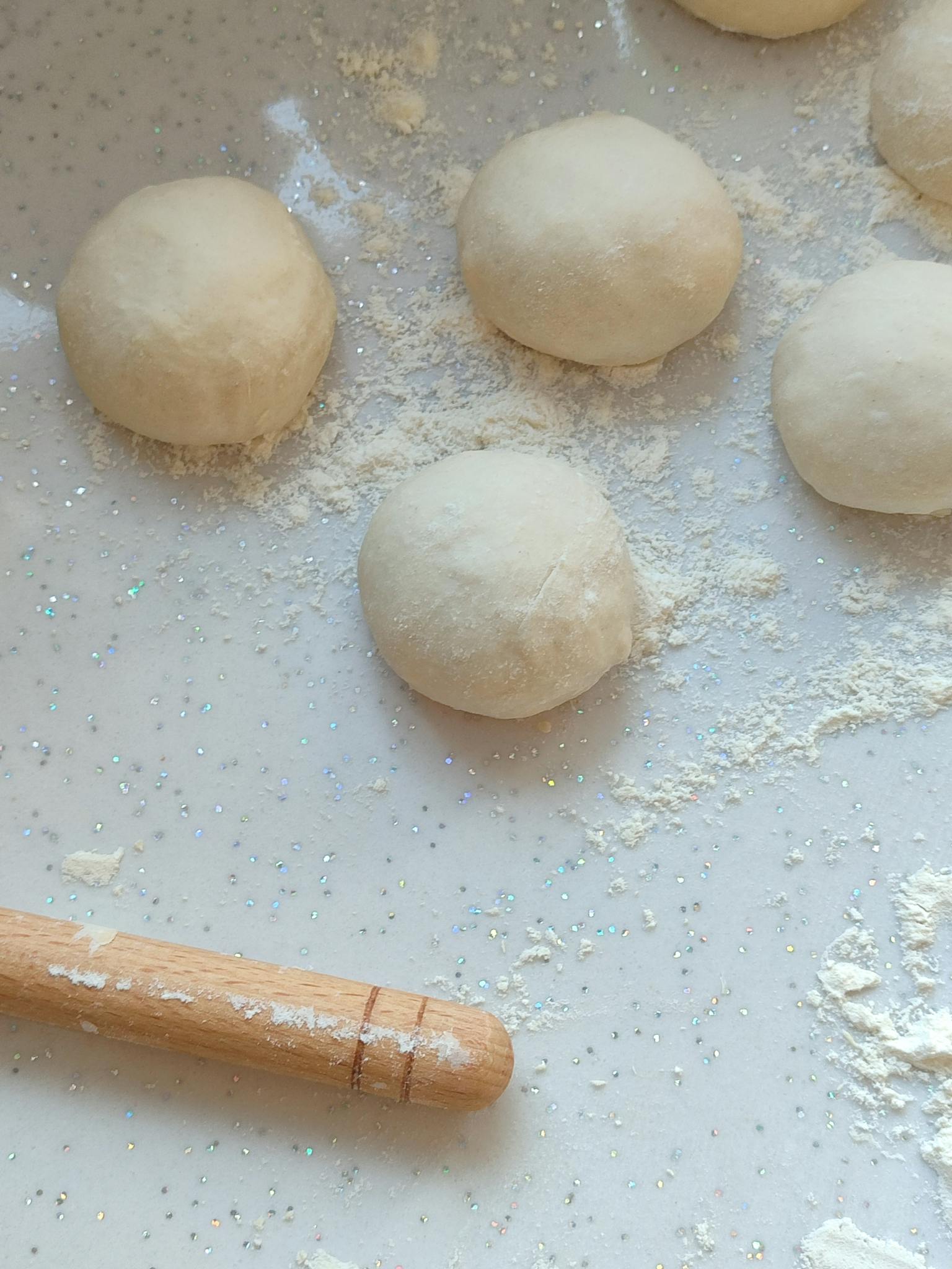 Close-up of pizza dough balls on a floured surface, ready for baking or cooking.