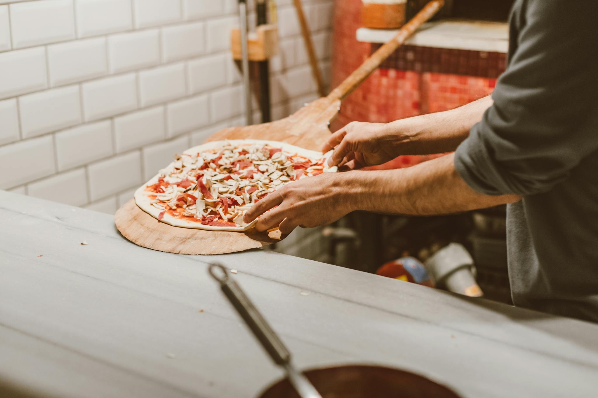Close-up of hands placing a pizza in a brick oven in a rustic kitchen.