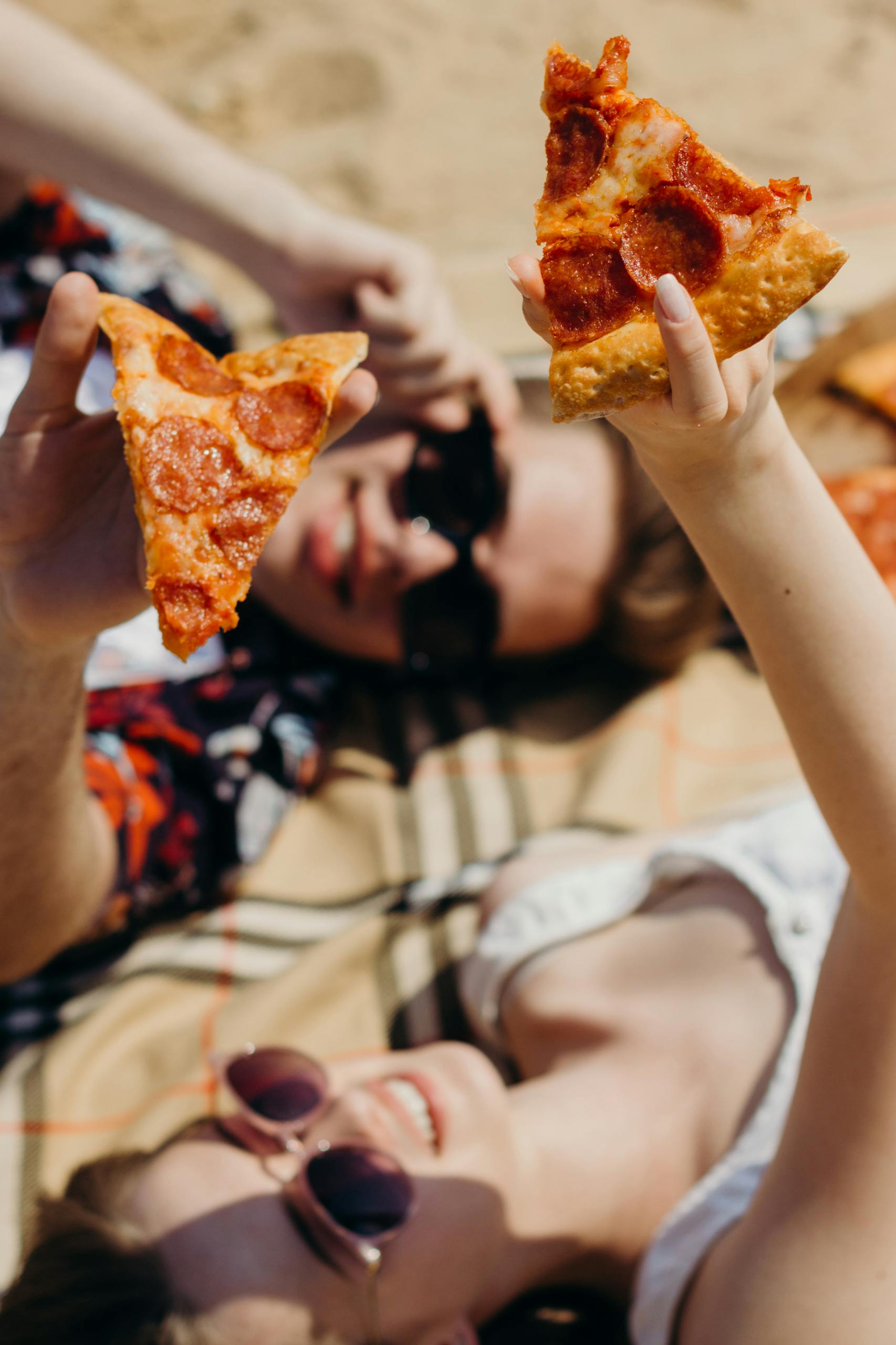 Two friends enjoying a sunny picnic with pepperoni pizza slices. Perfect summer outing.